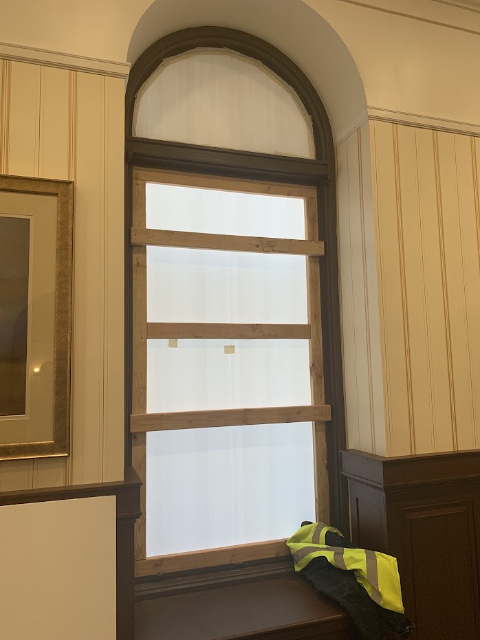 A mockup of a temporary window in the courthouse. It shows a wood frame with translucent white sheeting over the window that lets in light. The arch at the top of the window is blocked out.